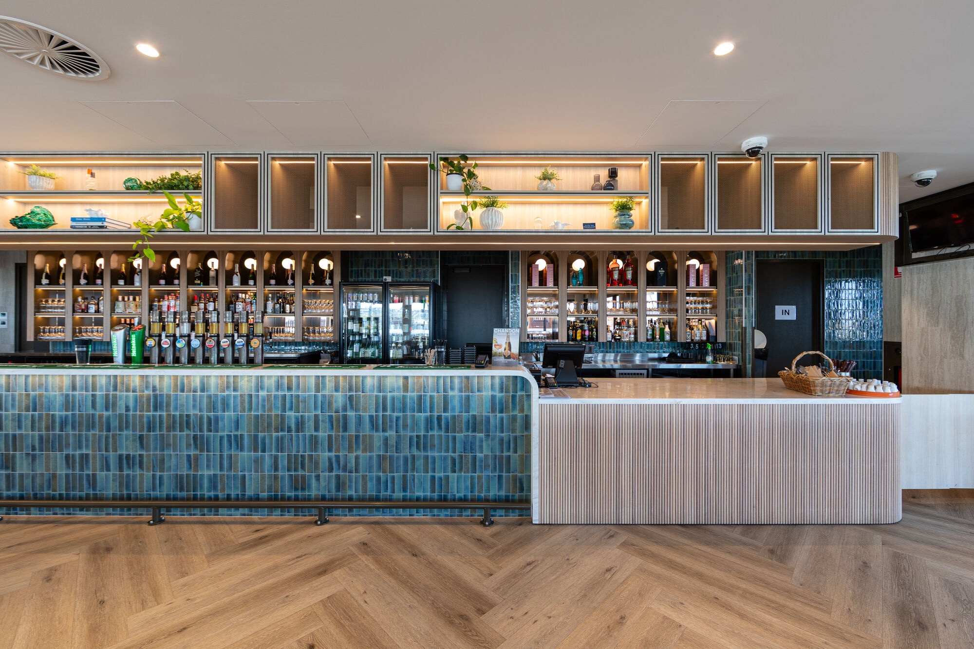 Interior bar at Ocean Reef Sea Sports Club with blue tiled counter, timber flooring, illuminated shelving and beverage displays.