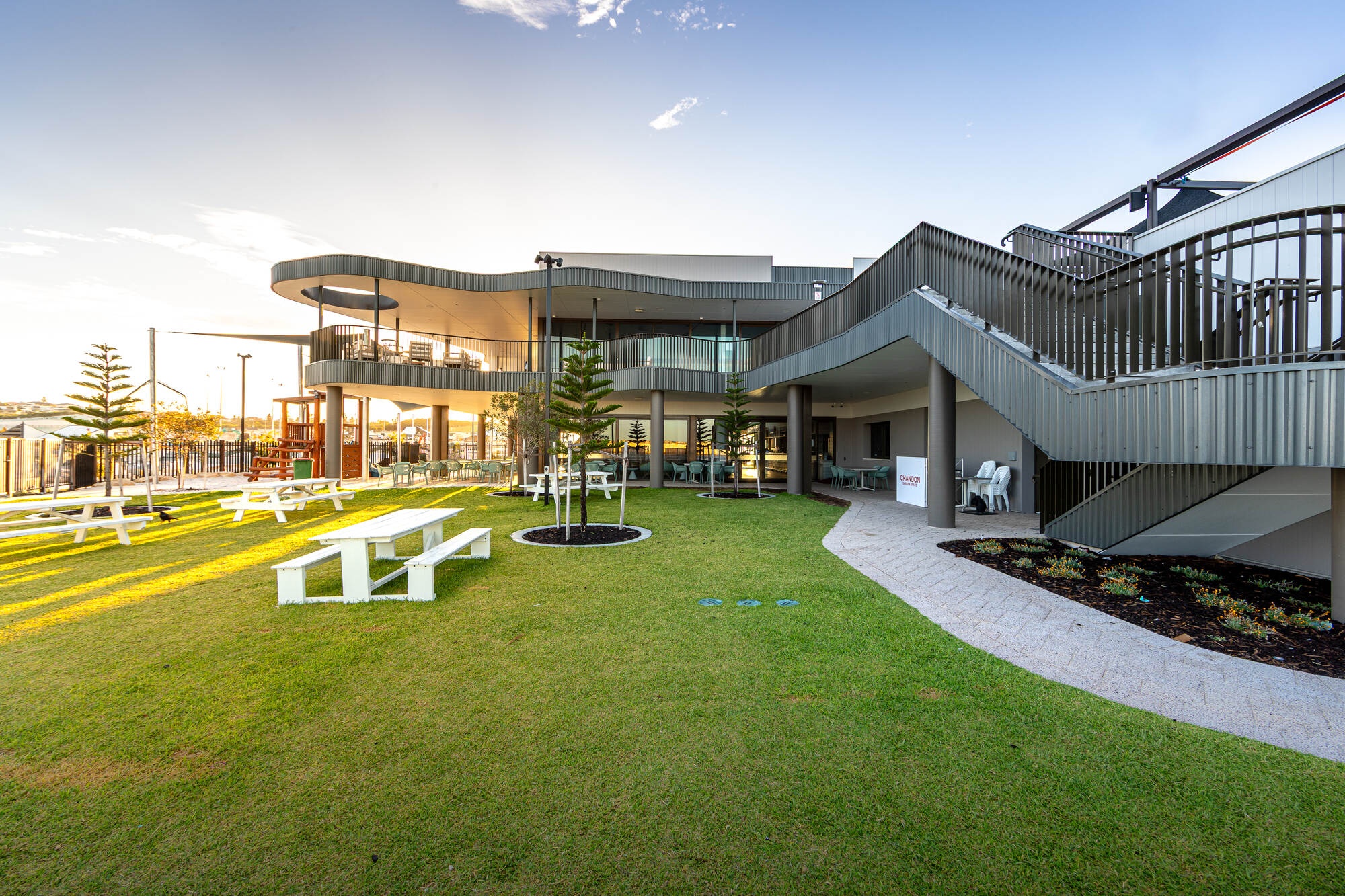 Landscaped outdoor area at Ocean Reef Sea Sports Club, showing lawn, picnic seating, balcony, stairs and the two-storey club building.